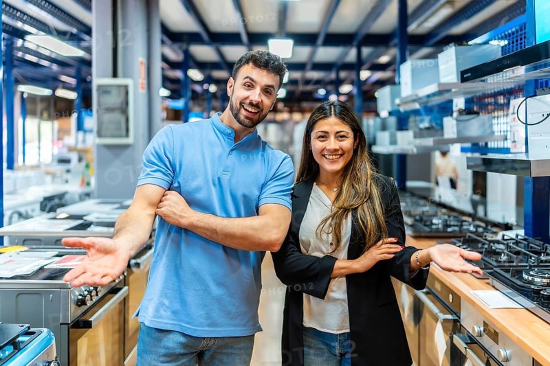 Smiling man and woman standing together in an appliance store showroom, welcoming potential buyers to explore kitchen renovations and home improvement options