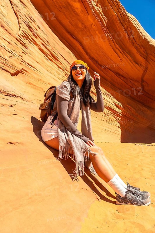 Woman traveler sitting in the desert sandstone formation of biidi the arch cave, enjoying her outdoor adventure and travel experience in page, arizona