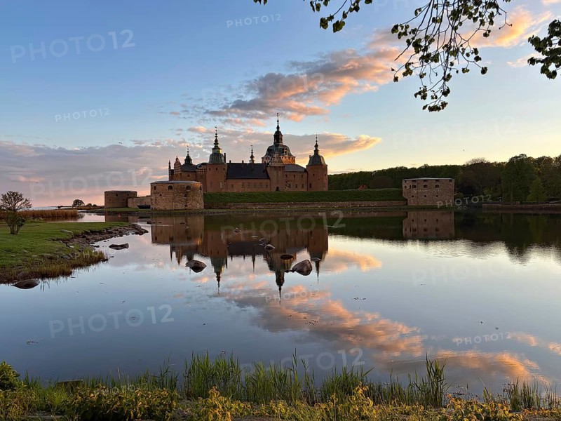 A castle is reflected in a calm lake, surrounded by colorful evening skies and peaceful nature, Kalmar Slott, Kalmar, Smaland, Sweden