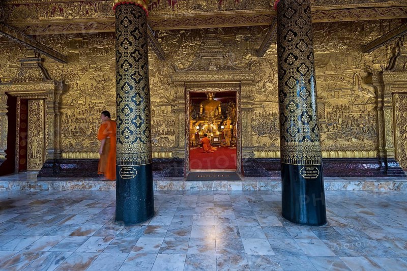 Buddhist monks and novices sit in front of a large Buddha statue in Wat May Souvannapoumaram, Luang Prabang, Laos, Southeast Asia