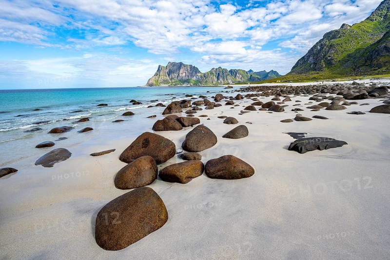 Rocks on the sandy beach of Uttakleiv, coast and blue sea, rocky mountain peaks, Vestvågøya, Lofoten, Nordland, Norway