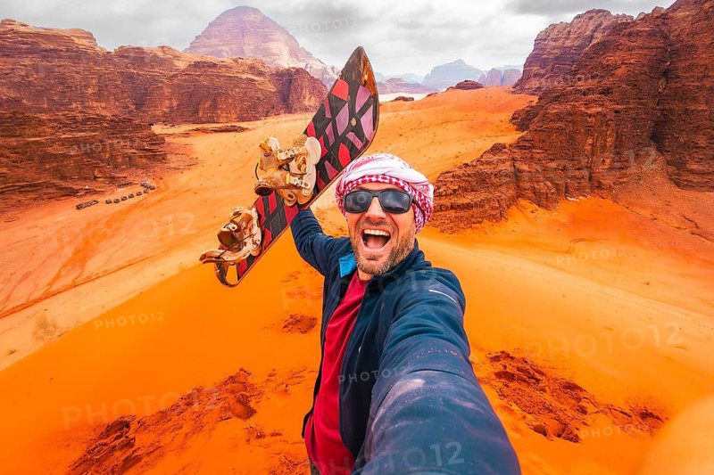Excited rider pov pose selfie from top viewpoint on big red dune in Wadi Rum desert Jordan. Sand boarding POV with board, desert adventure freedom concept. Wadi rum tours and Sandboarding activities
