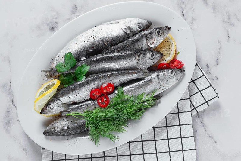 Fresh Herring fish, ready to cook, with herbs and spices, on a white platter, in the kitchen