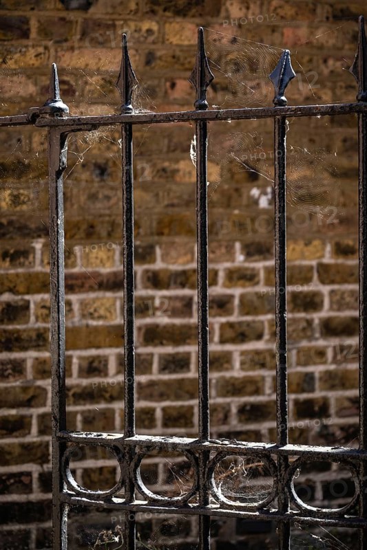 Old black painted metal fence with cobwebs in front of a weathered brick wall, Chelsea, London, Great Britain, England, Great Britain