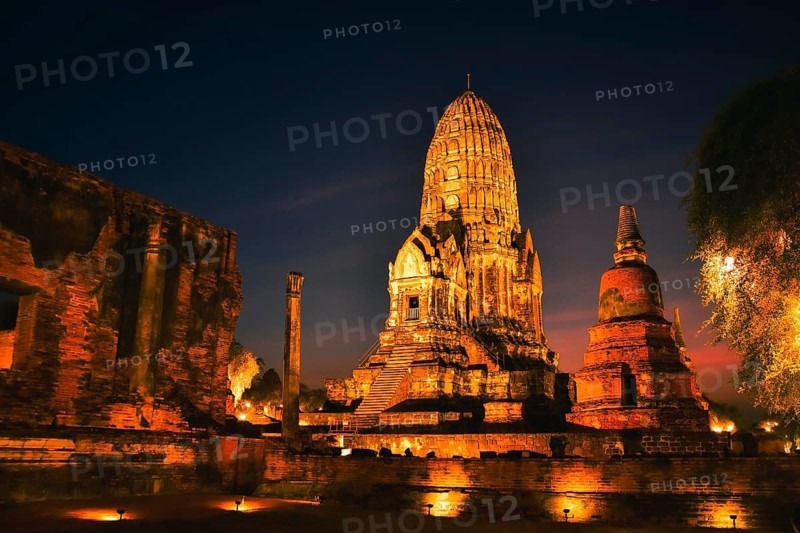 Wat Ratchaburana ancient temple in Ayutthaya Historical Park, Thailand .Towering central prang and crumbling brick ruins illuminated by warm golden lights against dark night blue hour sky