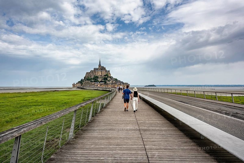 Tourists on the 760 meter long footbridge, Pont Passerelle, on the horizon the imposing rock island, Le Mont Saint Michel monastery island with the former Benedictine abbey in Norman style, tourist attraction, UNESCO World Heritage Site, Pontorson, Manche department, Normandy, France
