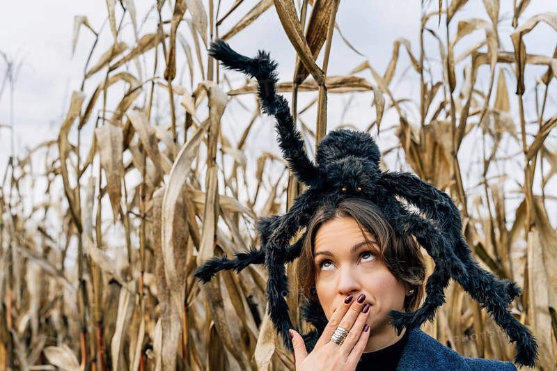 A woman covers her mouth with her hand in fear because of a toy large spider on her head. Halloween costumes and decorations