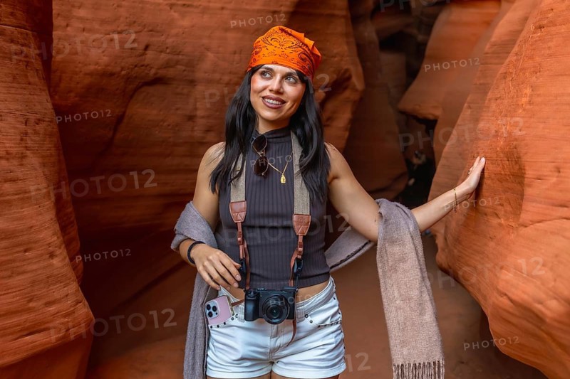 Woman traveler with camera explores antelope canyon's wavy red sandstone slot canyon in page, arizona, smiling as sunlight reveals textured, eroded rock formations and curves