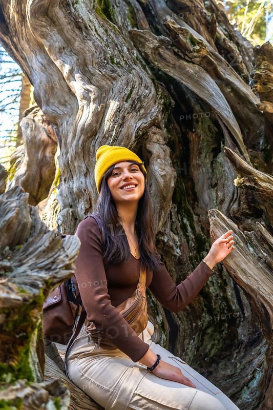 Happy young woman smiling, posing for a picture while sitting inside a massive ancient giant sequoia tree trunk, enjoying summer travel and outdoor recreation in nature