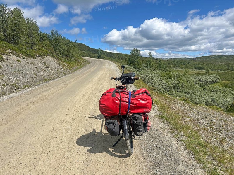 A bicycle with red bags is parked on a dirt road in the middle of green countryside, Peer Gynt Vegen, Norway