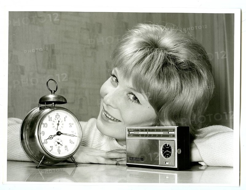 Transistor radio, with clock, versus alarm clock, advertising photography, smiling woman leaning at table with alarm clock and retro radio in a black and white portrait, Joachim Diederichs, around 1956