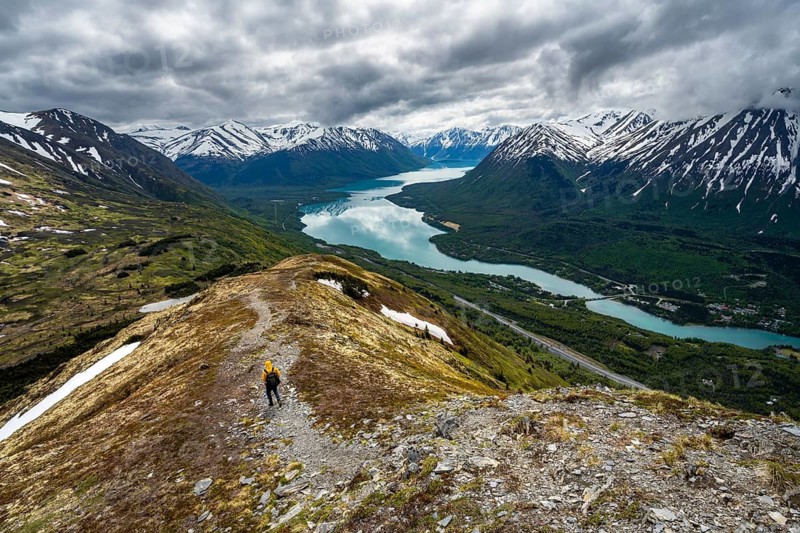 Climbers on a hiking trail on Slaughter Ridge, views of snowy mountains in spring and turquoise Lake Kenai Lake, Cooper Landing, Kenai Peninsula, Alaska, USA