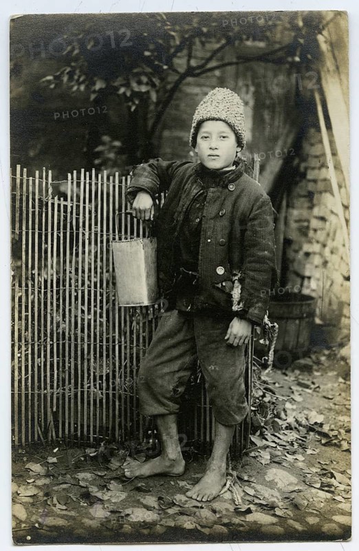 Polish boy, Vilnius, Lithuania, beggar, poverty, poverty, hunger, orphan, a boy leaning against a fence, holding a pot, barefoot and warmly dressed, atmosphere is calm, 1916