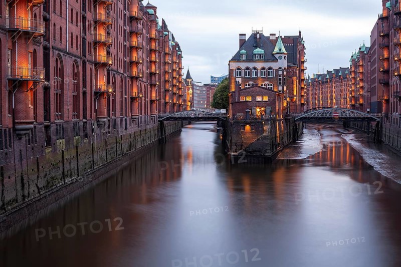 11.6.2018: Twilight view of the Wasserschloss (Water Castle) in the historic Speicherstadt district. The illuminated red brick warehouse complex and the canal are reflected in the water during the blue hour. UNESCO World Heritage site, Hamburg, Germany