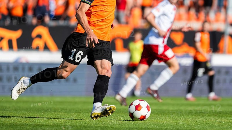 Soccer player in orange jersey number 16 running toward ball on green field during match, real authentic sports action in Glogow, Poland