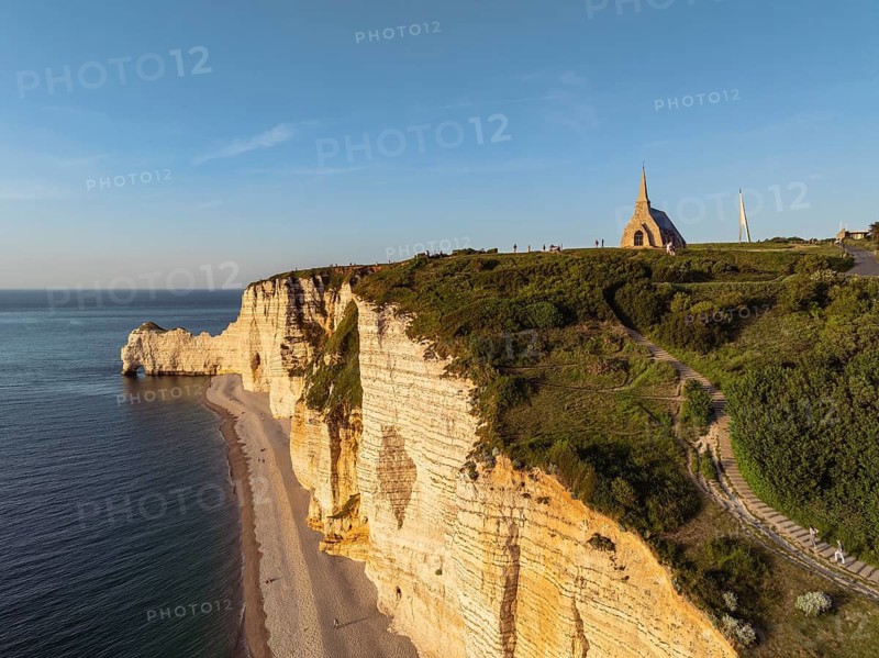 Aerial view of the Porte d'Amont rock formation and landmark, Falaise d'Amont in the evening sun with the Notre Dame de la Garde chapel, Étretat, Alabaster Coast, La Côte d'Albâtre, chalk cliffs, English Channel, Seine-Maritime, Normandy, France