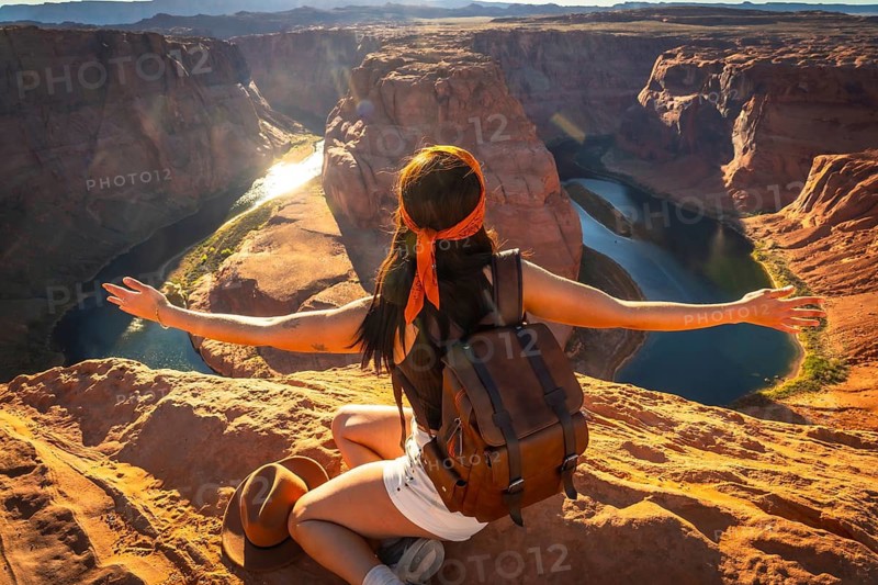 Woman with backpack raising arms in freedom and joy, admiring the breathtaking horseshoe bend canyon and colorado river vista during a solo travel adventure