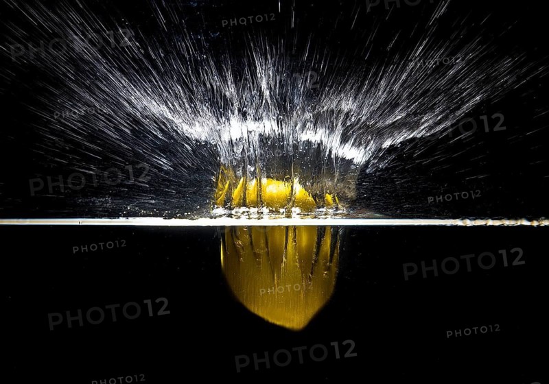 A fresh yellow lemon (Citrus limonum) falls into the water, creating a splash and air bubbles, against a black background