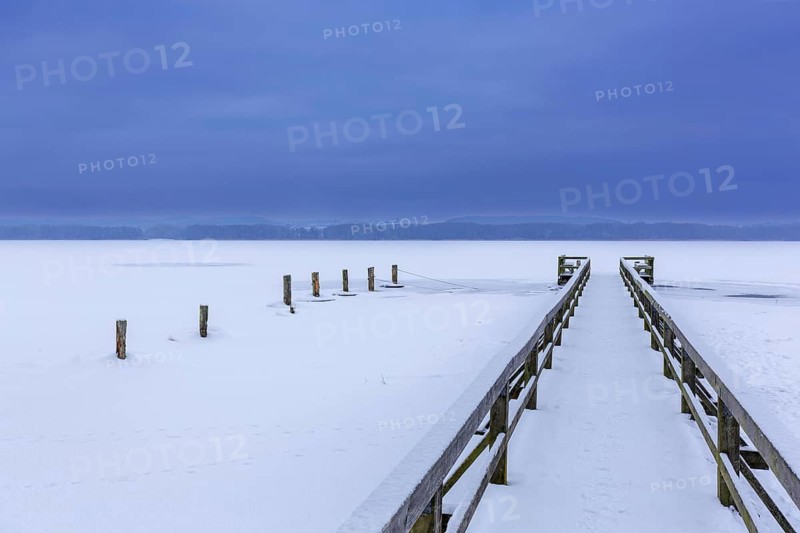Wooden jetty at frozen Lake Ratzeburg, Ratzeburger See covered in snow in winter, Lauenburg Lakes Nature Park, Schleswig-Holstein, Germany