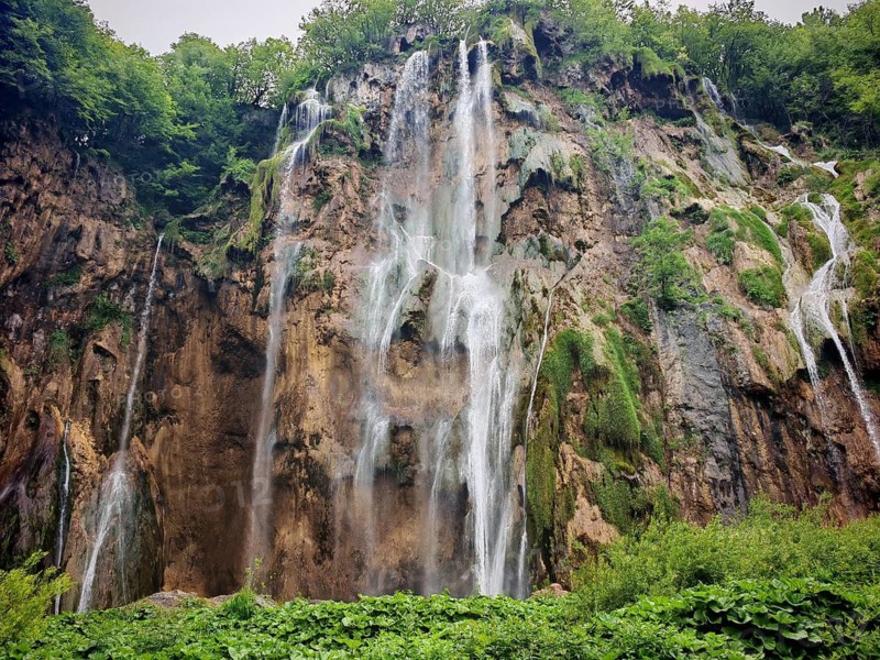 High waterfalls fall impressively over rocky cliffs and disappear into the dense forest, Plitvice Lakes National Park, Croatia