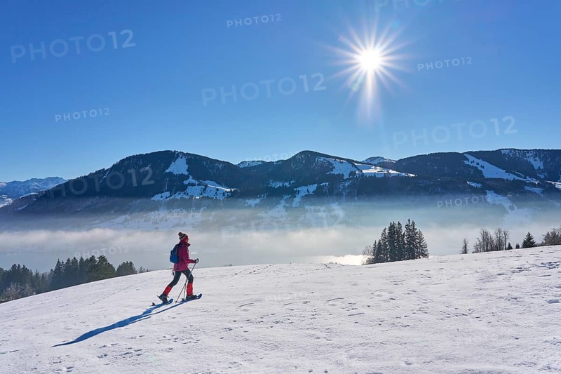 Sportive senior woman hiking with snow shoes in the snowy Allgaeu Alps above Lake Alosee, Immenstadt, Bavria, Germany