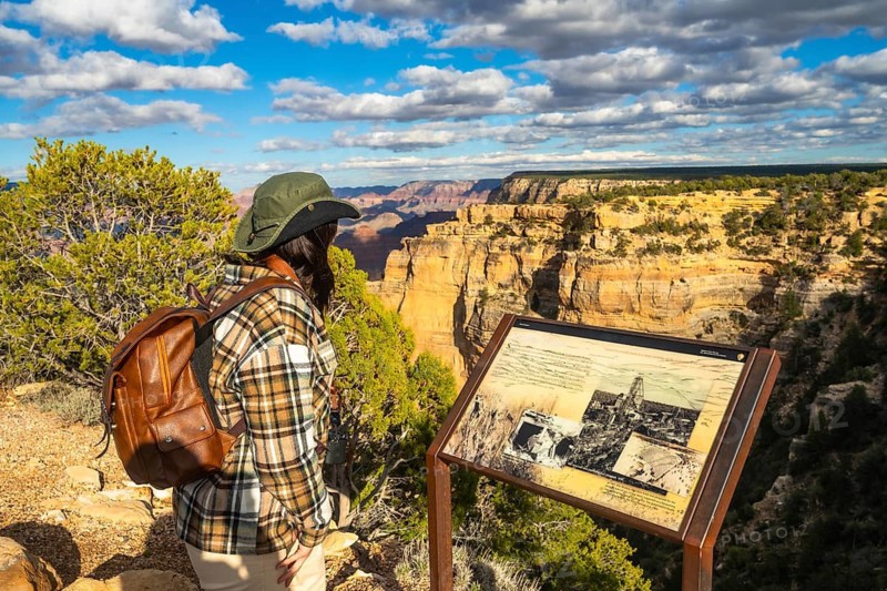 Traveler standing at a scenic viewpoint, observing the vast, layered rock formations and natural beauty of the grand canyon under a dynamic cloudy sky