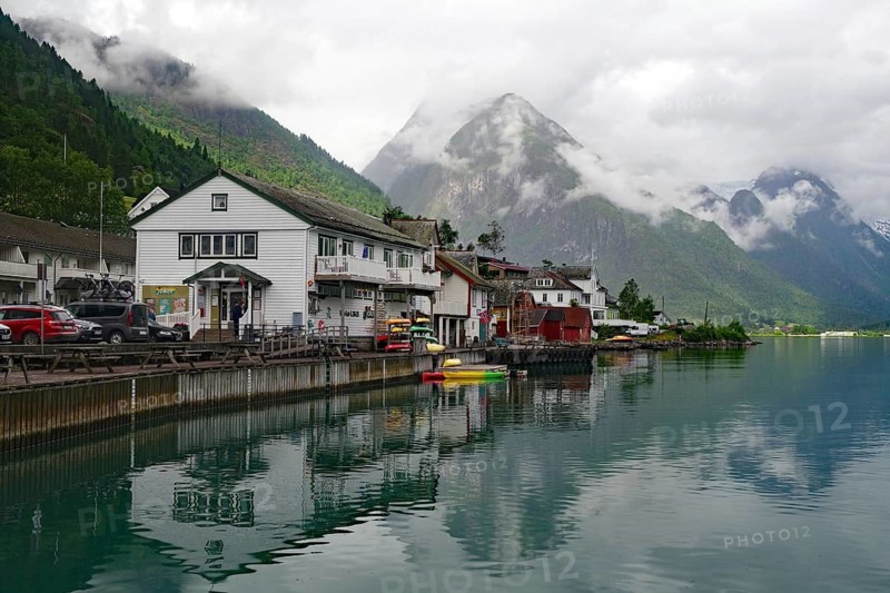 A quiet lakeside village with mountains in the background under a cloudy sky, Bücherdorf, Fjaerland, Norway