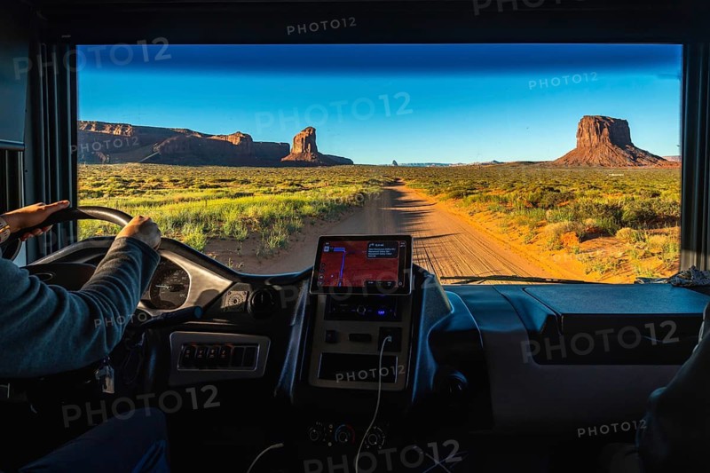 Person driving a recreational vehicle on a dirt road, experiencing a desert road trip through monument valley's scenic buttes and vast landscape during a warm sunrise