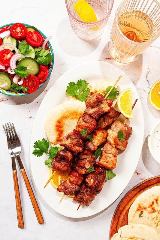 Souvlaki, a Greek dish, grilled meat shish kebab, on a plate with flatbreads, and lemon slices, grilled meat shish kebab, served with lavash, salad and drinks where there are no people