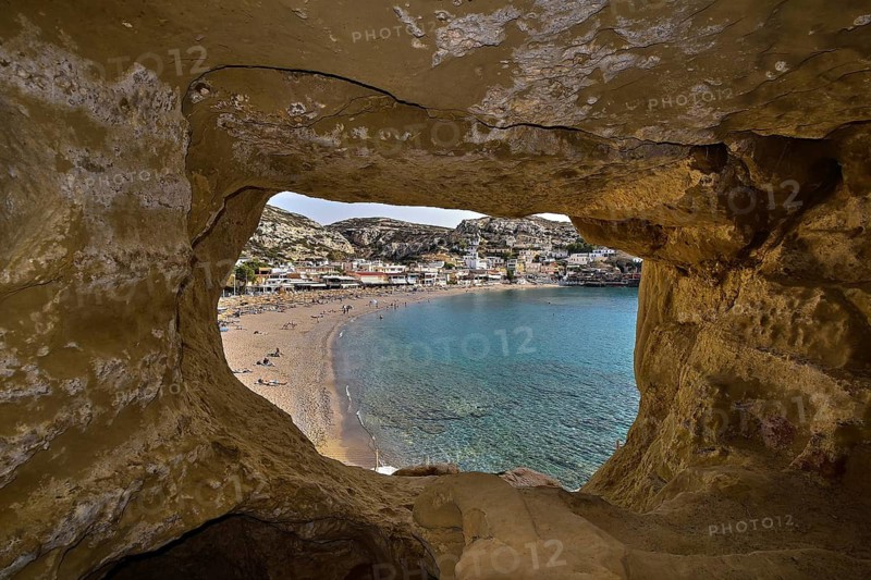 View through a rock cave of a coastal village with beach and blue sea, Matala, Neolithic caves, former hippie paradise, central south coast, Crete, Greek Islands, Greece