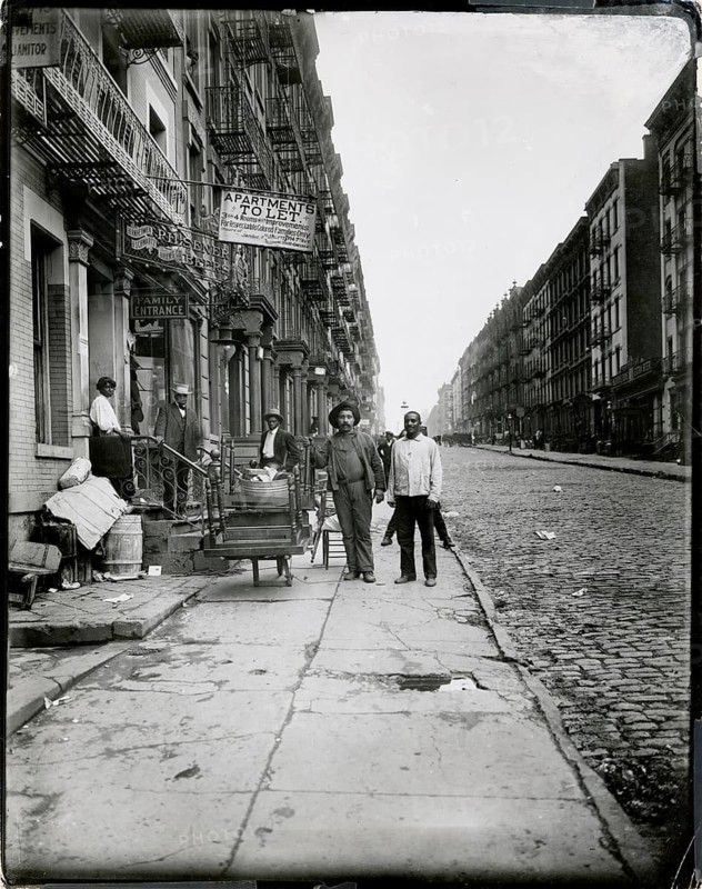 New York, West 103th Street_Apartment for rent for respectable Negro family, poverty, black, Harlem, African-American, people standing on a sidewalk of a busy street in a historic city environment, 1915