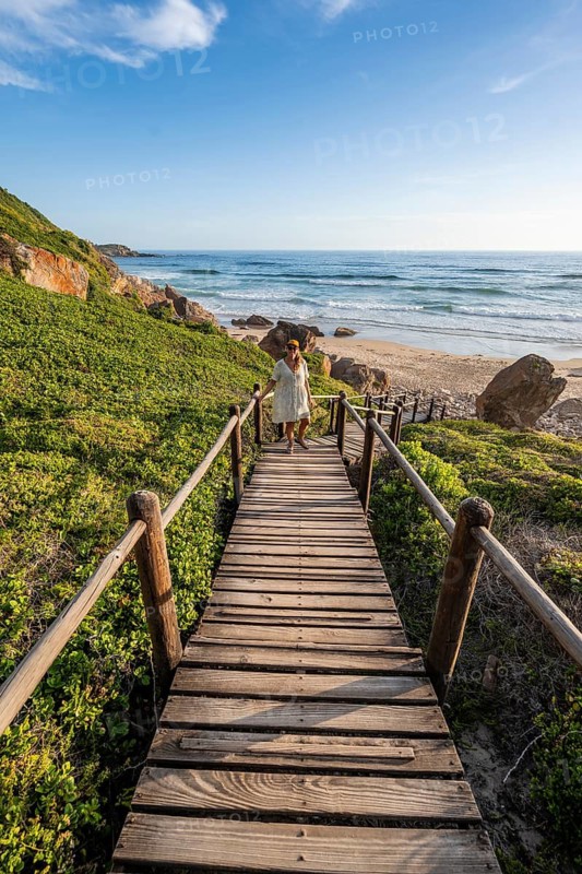 Young pretty woman wearing dress off coast and sea at Robberg Nature Reserve, Plettenberg Bay, South Africa