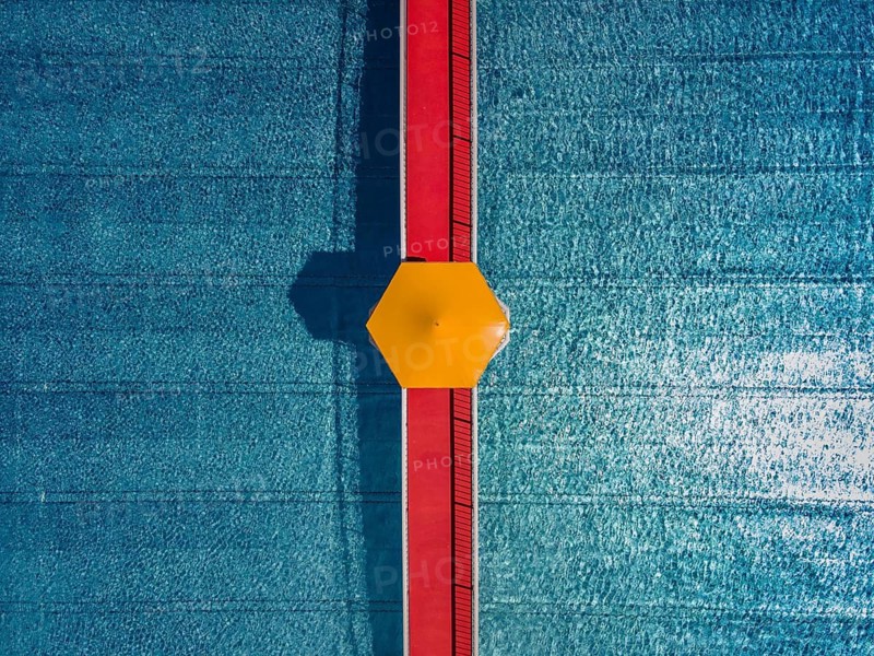 On a red bridge spanning a swimming pool at an open-air lido in Frankfurt, there is a yellow parasol in the centre. The deserted pool below is still waiting for the rush of bathers. The start of the swimming season is just around the corner. (Aerial view taken by drone), Eschersheim, Frankfurt am Main, Hesse, Germany