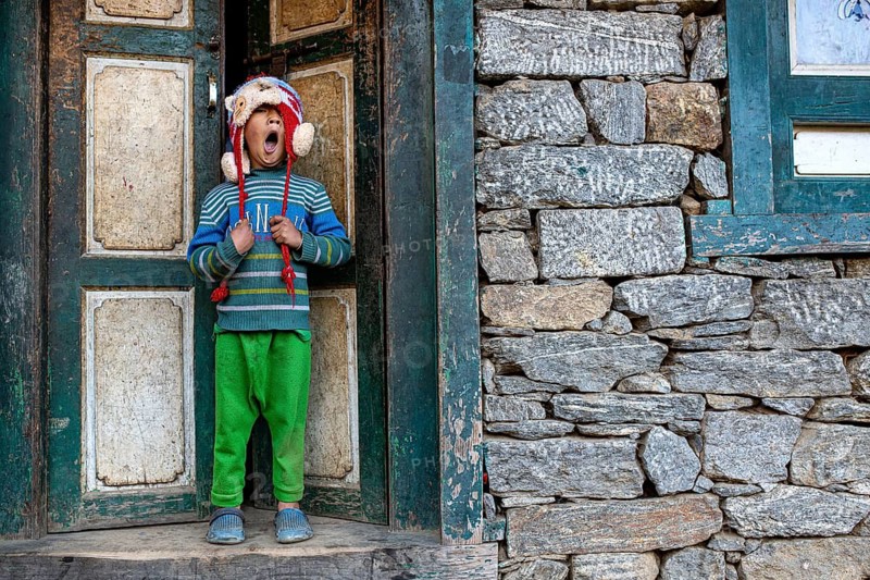 Little Nepalese boy from the Sherpa ethnic group yawning in front of a front door, Solu Khumbu Everest region, Himalayas, Nepal