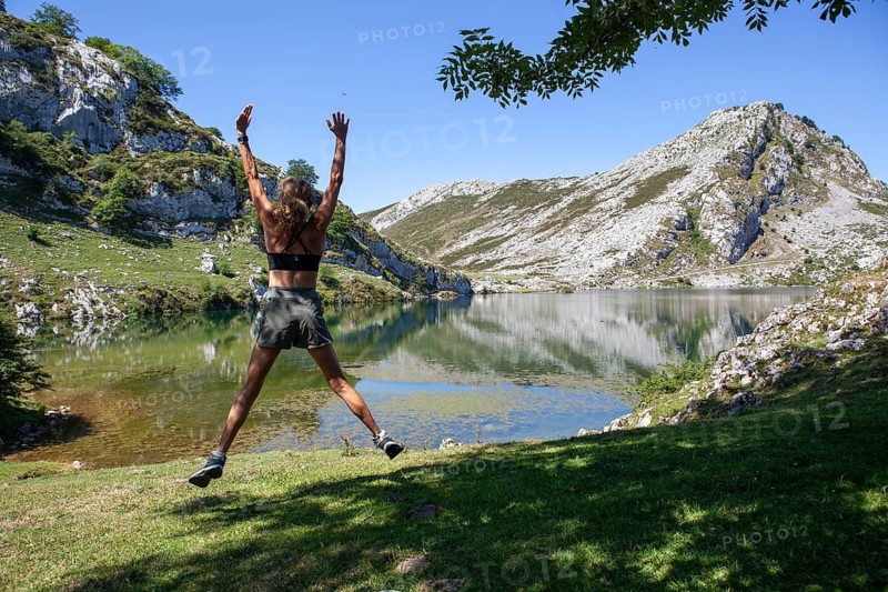 Middle aged woman jumps in front of Ercina lake, Covadonga lakes ensemble, Picos de Europa National Park, principality of Asturias, Spain