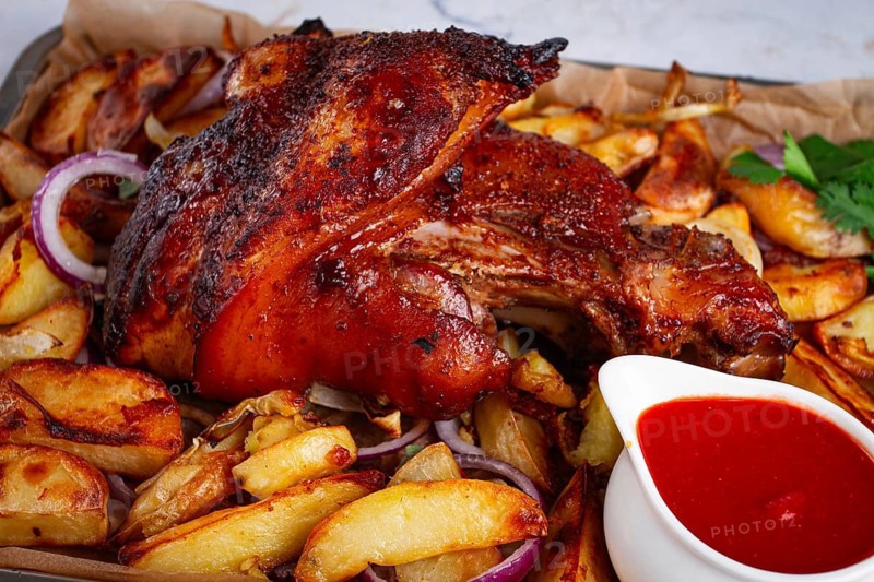 Baked pork knuckle, with potato slices, on a tray, with red sauce, homemade, no people, light background