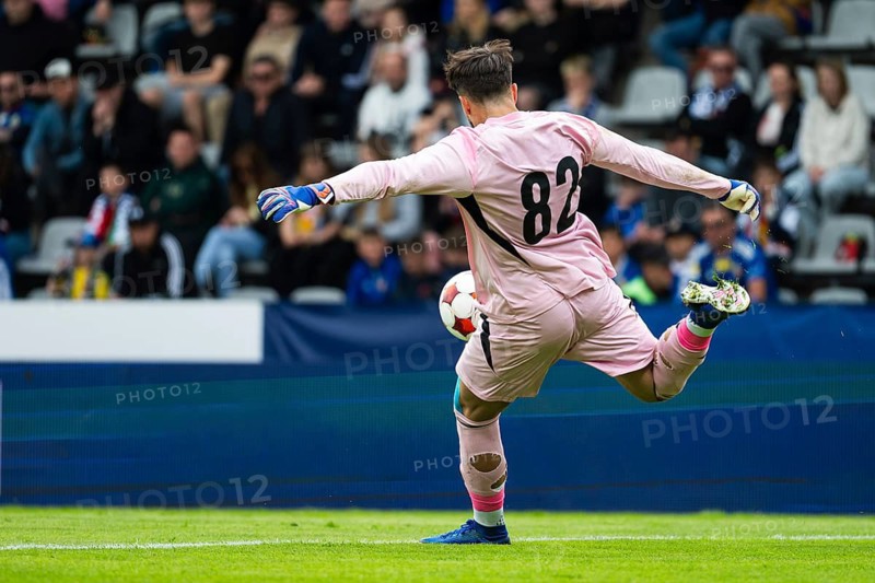 Goalkeeper in pink kit kicking the ball during a football match in a crowded stadium, dynamic sports action captured from behind in Legnica, Poland