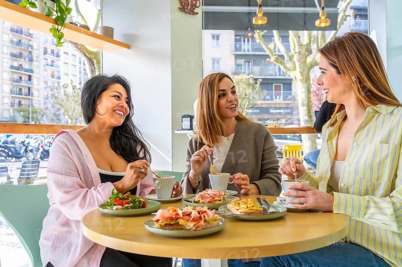 Women friends spending time together, sitting around a table in a modern cafe, drinking coffee and eating open faced sandwiches, enjoying conversation and a social gathering