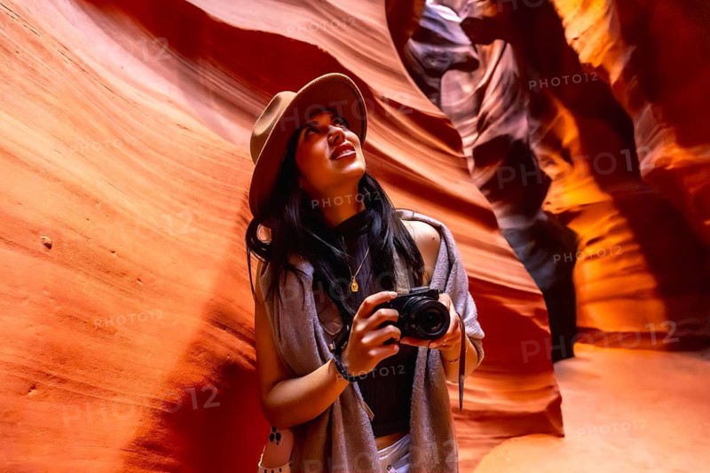 Young woman looking up at the illuminated sandstone walls of antelope canyon with a camera, capturing the unique geological formations and light during her solo travel adventure