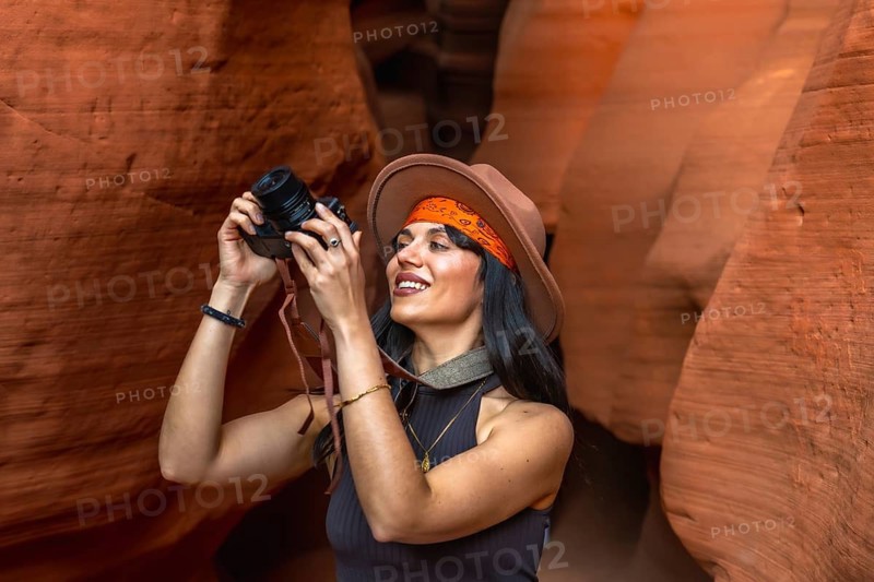 Woman traveler exploring the slot canyon, holding a camera and capturing moments of the unique sandstone textures and swirling patterns, discovering natural beauty during her adventure