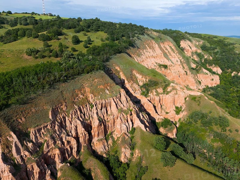 Red rock walls in a green hilly landscape with clear erosion patterns and dense forests, aerial view, Râpa Ro?ie, Rapa Rosie, Red Gorge, nature reserve, Sebe?, Alba County, Transylvania, Romania