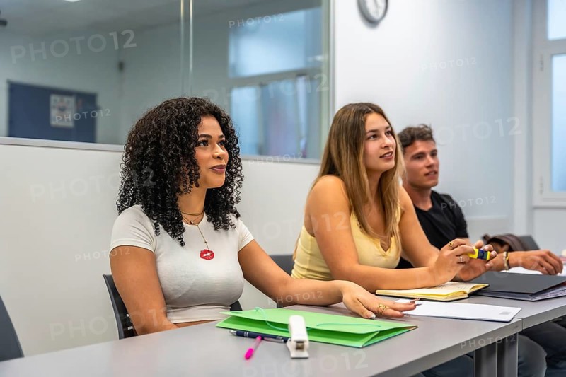 Young diverse students sitting at desks, listening attentively and participating in an academic lecture or seminar in a contemporary university classroom