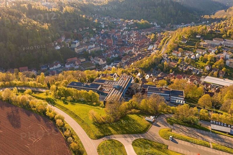 Aerial view of a village in a hilly, green landscape, roads and fields visible in sunshine, Calw District Office, Calw District, Germany