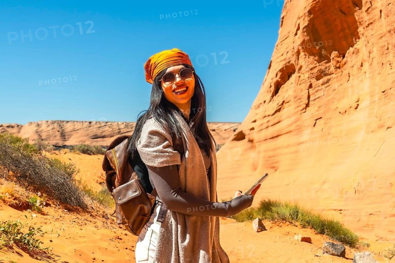 Young woman smiling and holding a mobile phone, experiencing a solo desert adventure while exploring the scenic sandstone canyons near biidi the arch cave in page, arizona