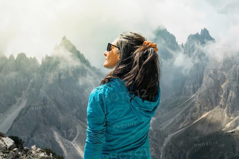 Close up profile woman hiker in turquoise fleece holding hair looking at dramatic mist covered mountain peaks background Cadini di Misurina Dolomites Italy summer