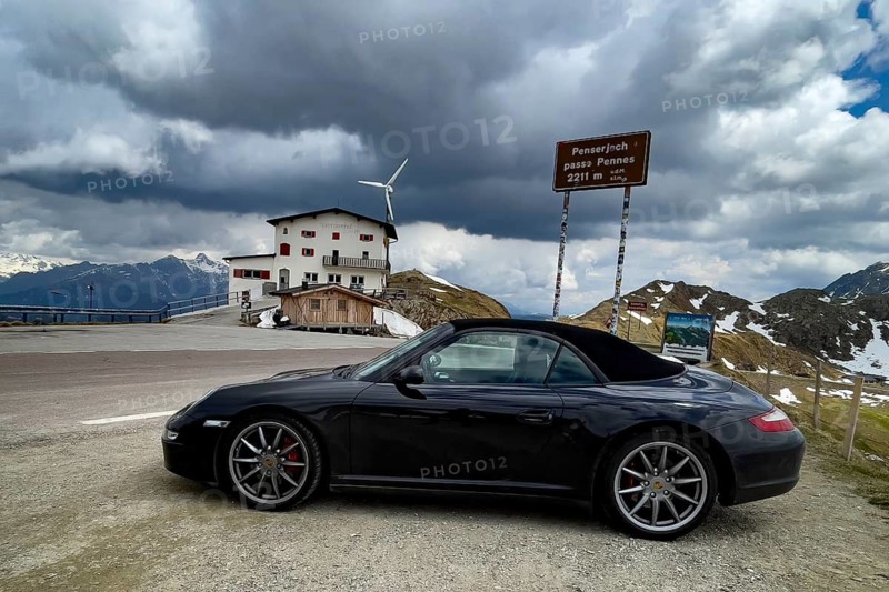 Porsche 911 Carrera 4s cabriolet 997 Convertible Car stands at pass height from mountain pass in Alpen Pass road in front of sign Penser Joch Penserjoch Passo di Pennes with altitude 2211 meters m, South Tyrol, Italy