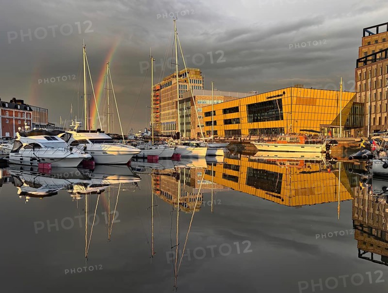 Modern buildings and boats are reflected in harbor water under a dramatic sky with rainbow, University, Kalmar, Smaland, Sweden