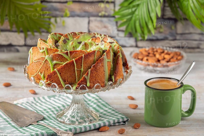 A cake with green icing next to a cup of coffee and almonds