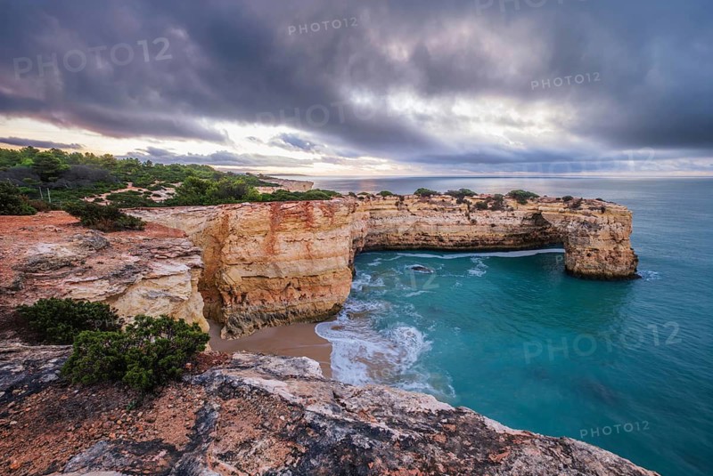 Stormy sunrise scene at Praia de Albandeira beach in Algarve, Portugal, with Arco de Albandeira, ocean water and dark clouds