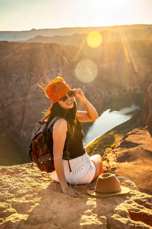 Woman backpacker sitting on a rock admiring the stunning panoramic view of horseshoe bend canyon, the colorado river, and surrounding desert landscape at golden hour